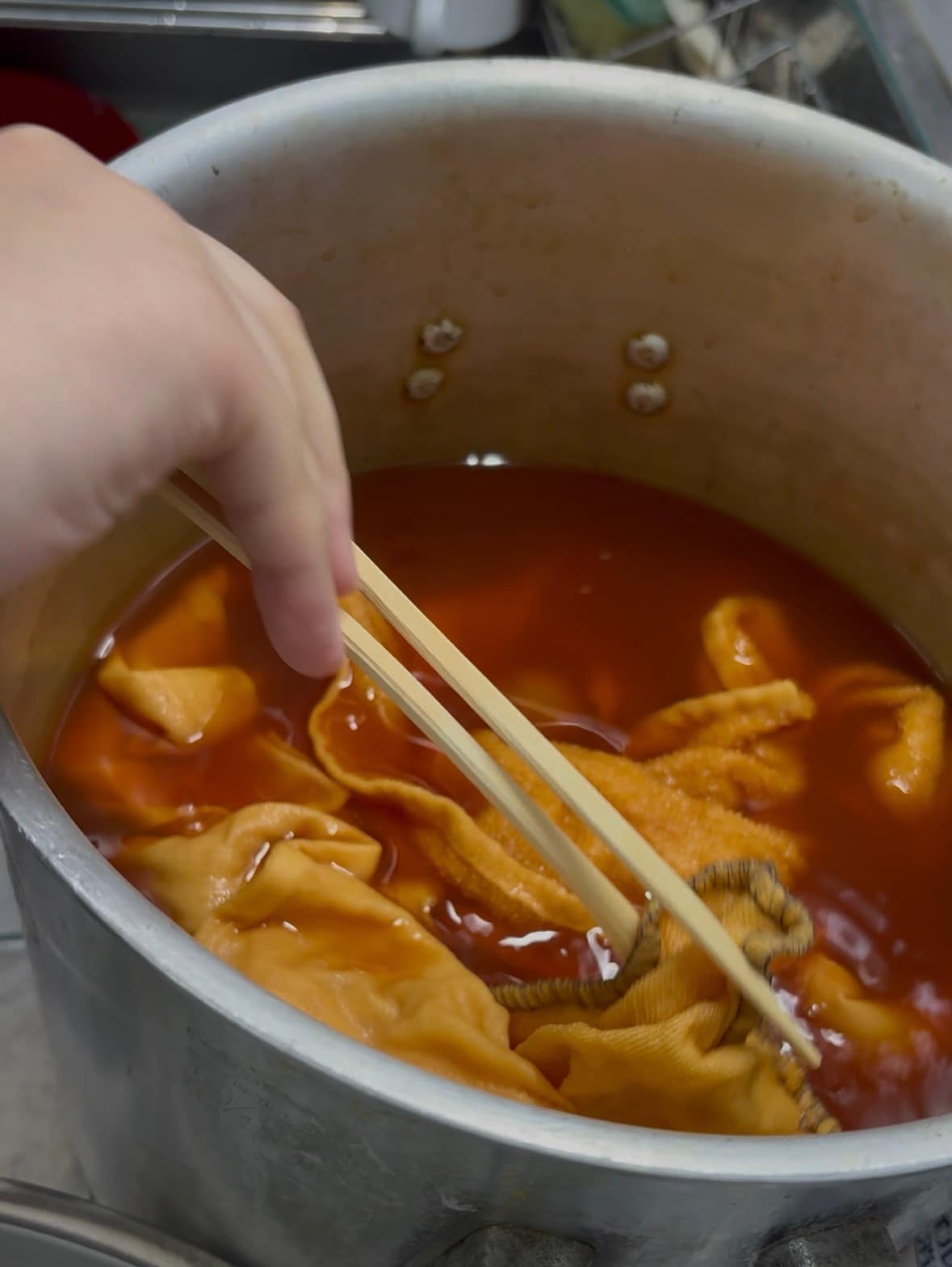 鍋の中の料理をのぞきこむ手元