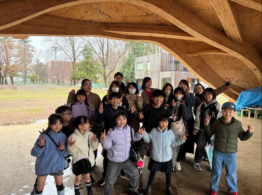 大学の木の大屋根の下に集まった子どもたちの集合写真